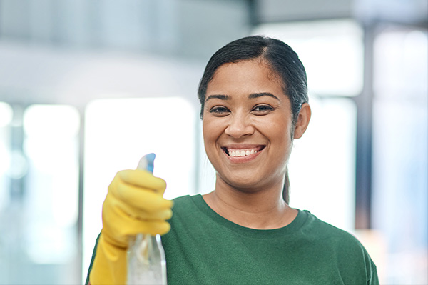 Smiling cleaning services worker in yellow rubber gloves holding a spray glass cleaner