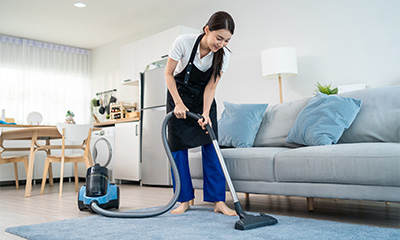 Young woman from cleaning services staff vacuuming the carpet