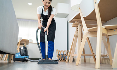 Young woman from the cleaning staff vacuuming the floor