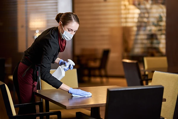 Cleaning girl in sterile gloves and protective mask dusting off the table