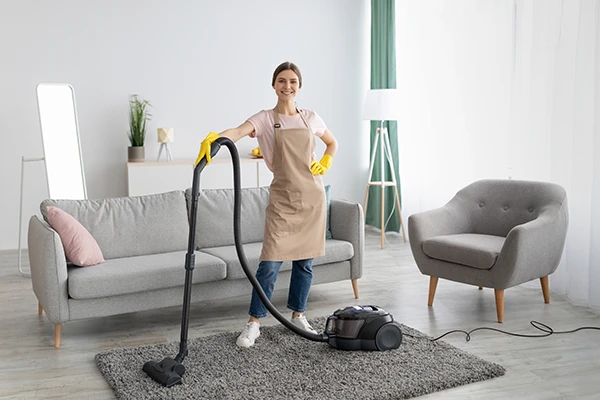 Smiling cleaning service worker vacuuming the carpet