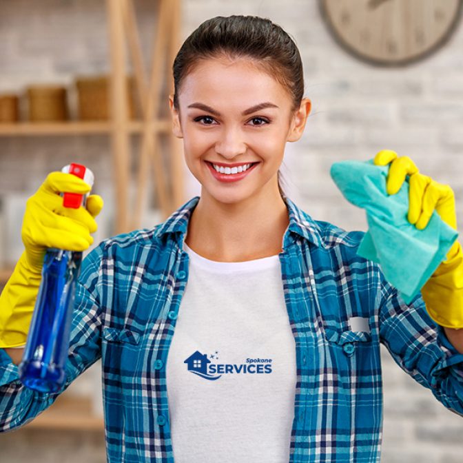 Smiling cleaning services worker in yellow rubber gloves holding a rag and a glass cleaner